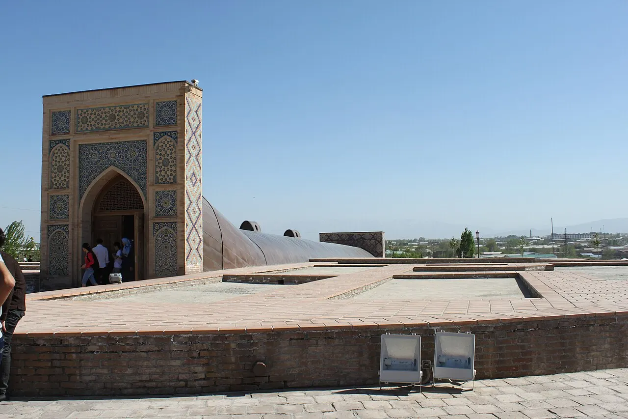 Portal revestido de azulejos e base do Observatório de Ulugh Beg, sob céu claro, com visitantes à esquerda.