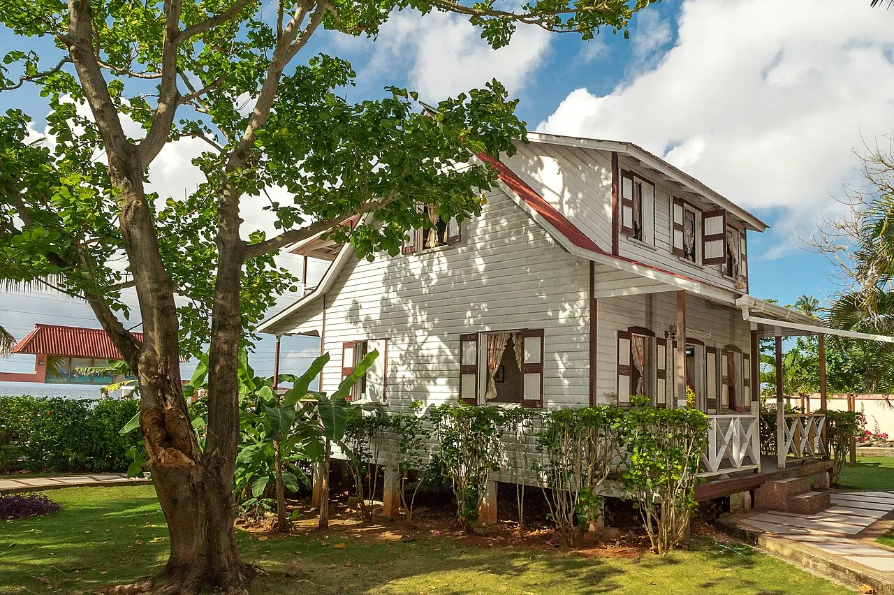 A Casa Museo Isleña, uma casa de madeira branca de dois andares com varanda e telhado vermelho, à sombra de uma árvore no gramado.
