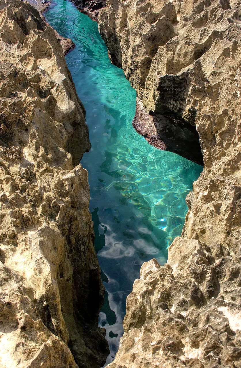 Canal estreito na costa rochosa do Hoyo Soplador, com água turquesa entre as paredes escuras de coral.