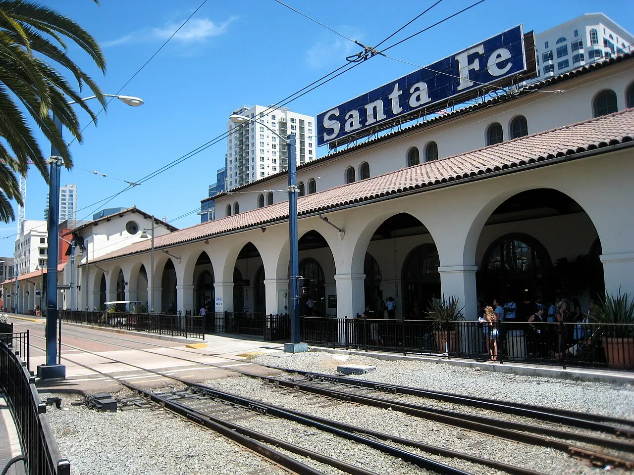 Estação ferroviária de arcos brancos e telhado de telhas com letreiro «Santa Fe» no alto, trilhos em primeiro plano