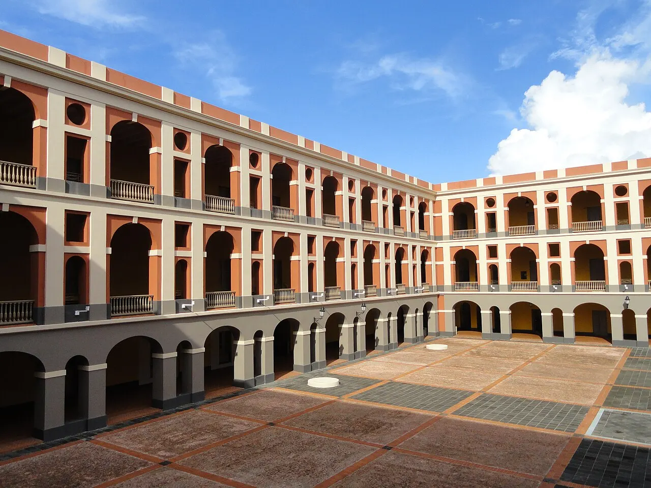 Pátio interno do edifício que abriga o Museo de las Américas, com três andares de arcadas em terracota e branco em volta de um piso quadriculado