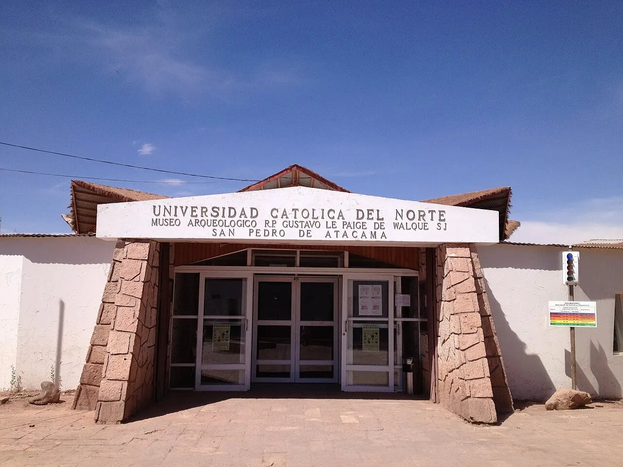A entrada do Museu Arqueológico Gustavo Le Paige, em San Pedro de Atacama, com portas de vidro, pilares de pedra e o letreiro da Universidad Católica del Norte.
