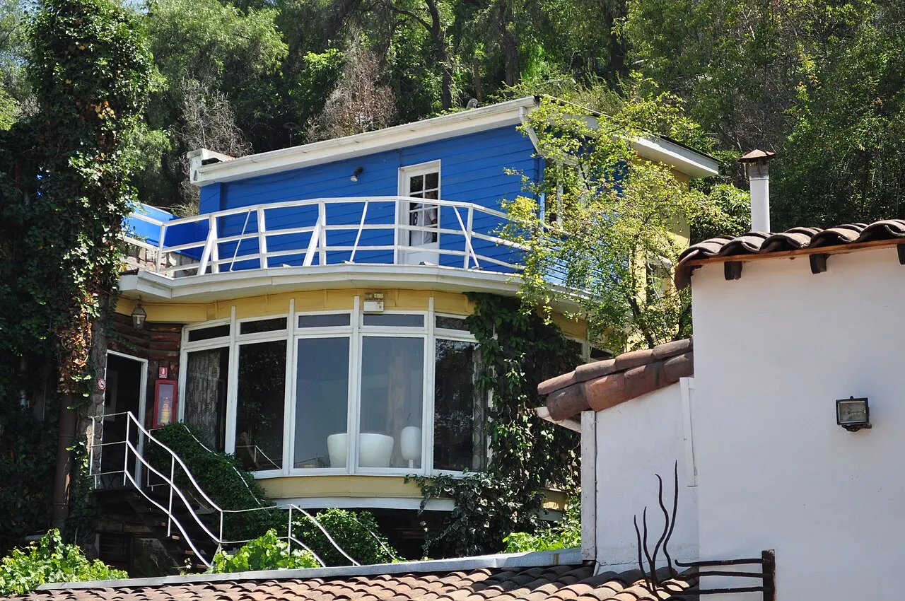 A casa azul de La Chascona, com varanda de grade branca, entre árvores e muros brancos.