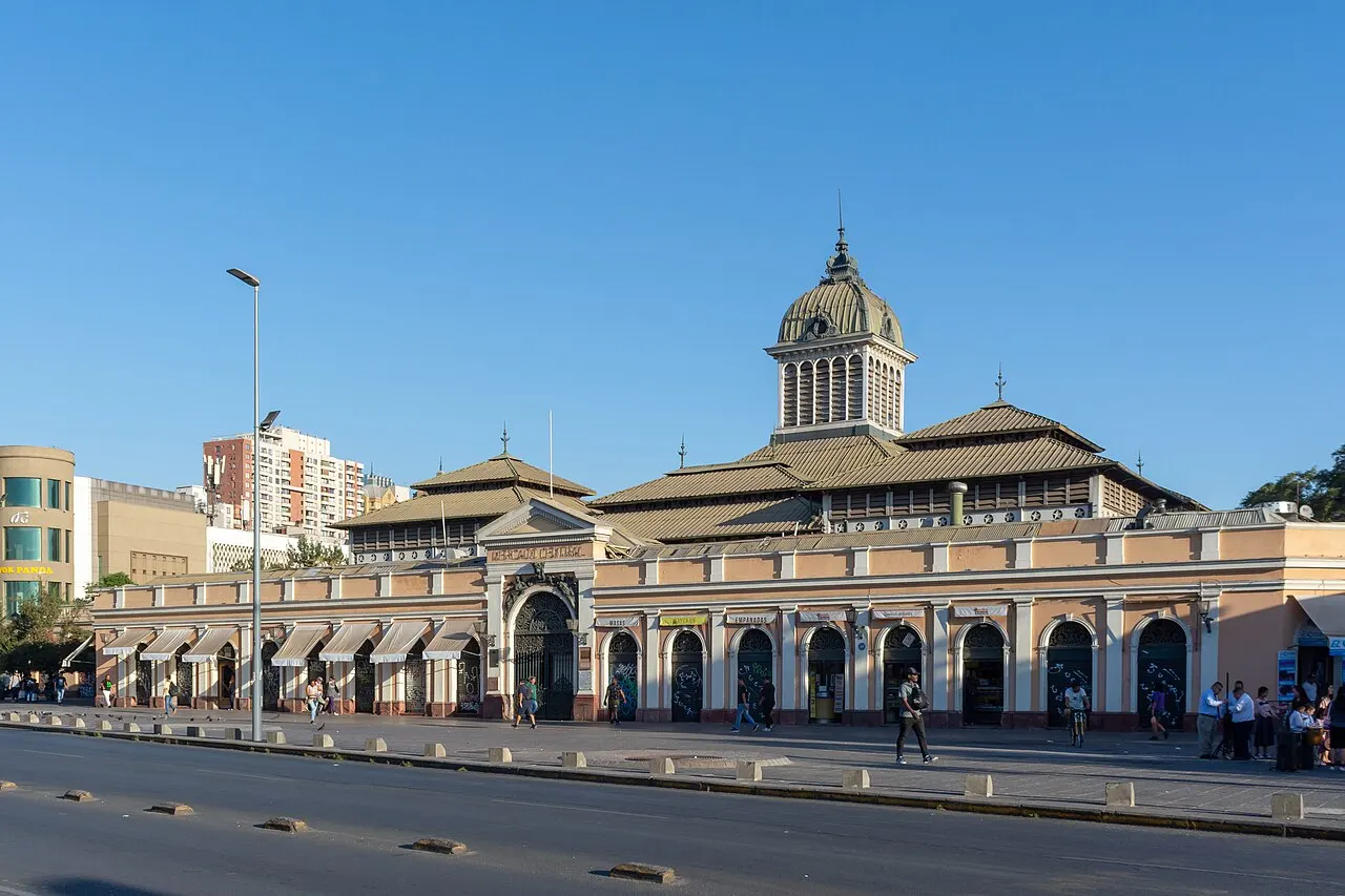 Prédio do Mercado Central, com pequena cúpula e arcadas ao longo da rua, sob céu azul.