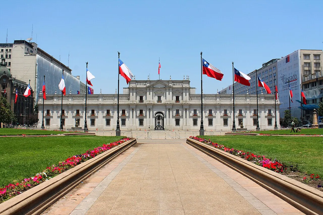 O Palacio de La Moneda visto de frente, com bandeiras chilenas e canteiros floridos ao longo da alameda.
