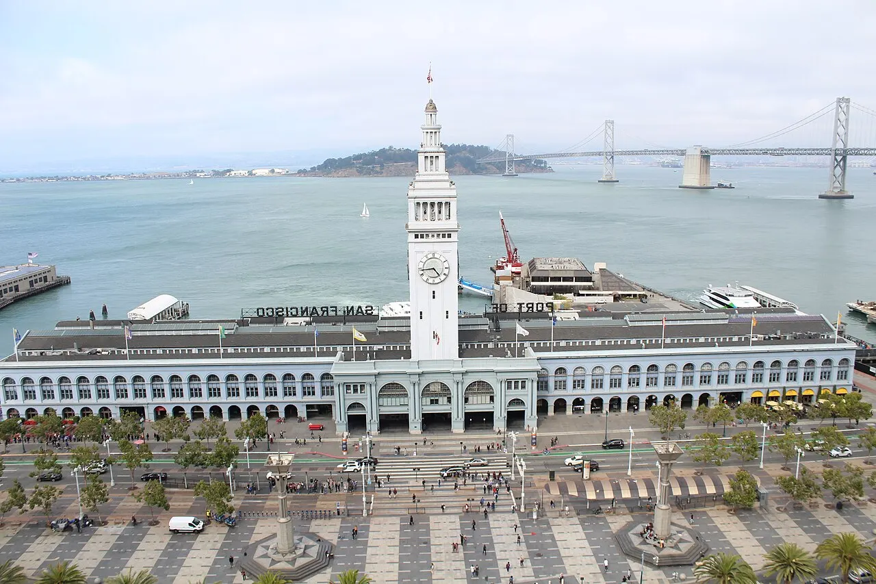 Ferry Building de São Francisco, comprido, com a torre do relógio ao centro, à beira da baía.
