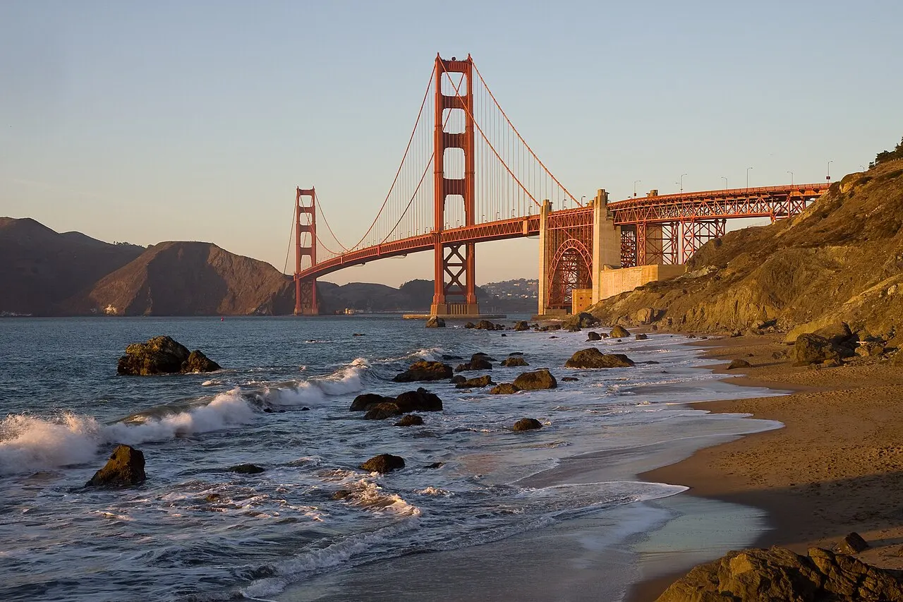 Golden Gate Bridge vista da praia, com as duas torres vermelhas e o vão suspenso sobre a água.