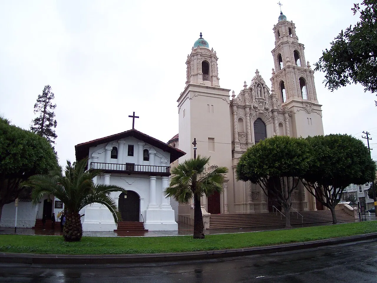 Missão Dolores e a basílica ao lado, em São Francisco, com fachadas brancas e palmeiras à frente.
