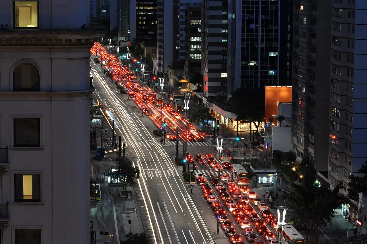 Avenida com o trânsito de noite e a fileira de prédios dos dois lados.