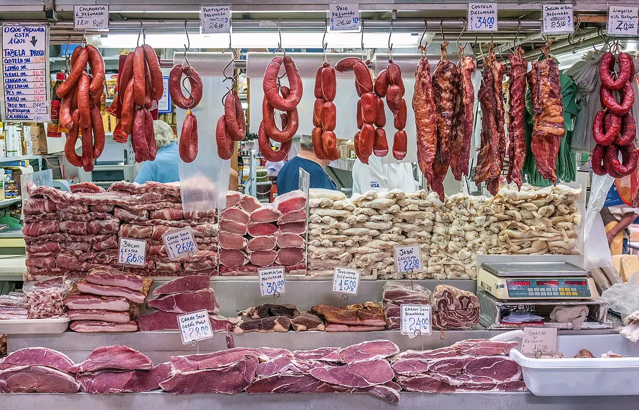 Banca do Mercado Municipal com linguiças penduradas no alto e cortes de carne expostos no balcão.