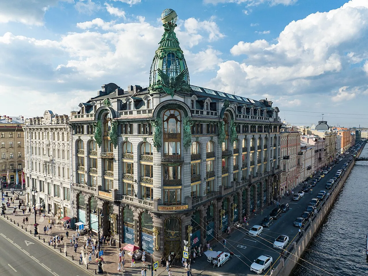 Casa Singer, na Avenida Nevsky, em São Petersburgo, com a cúpula de vidro na esquina, sob céu azul.