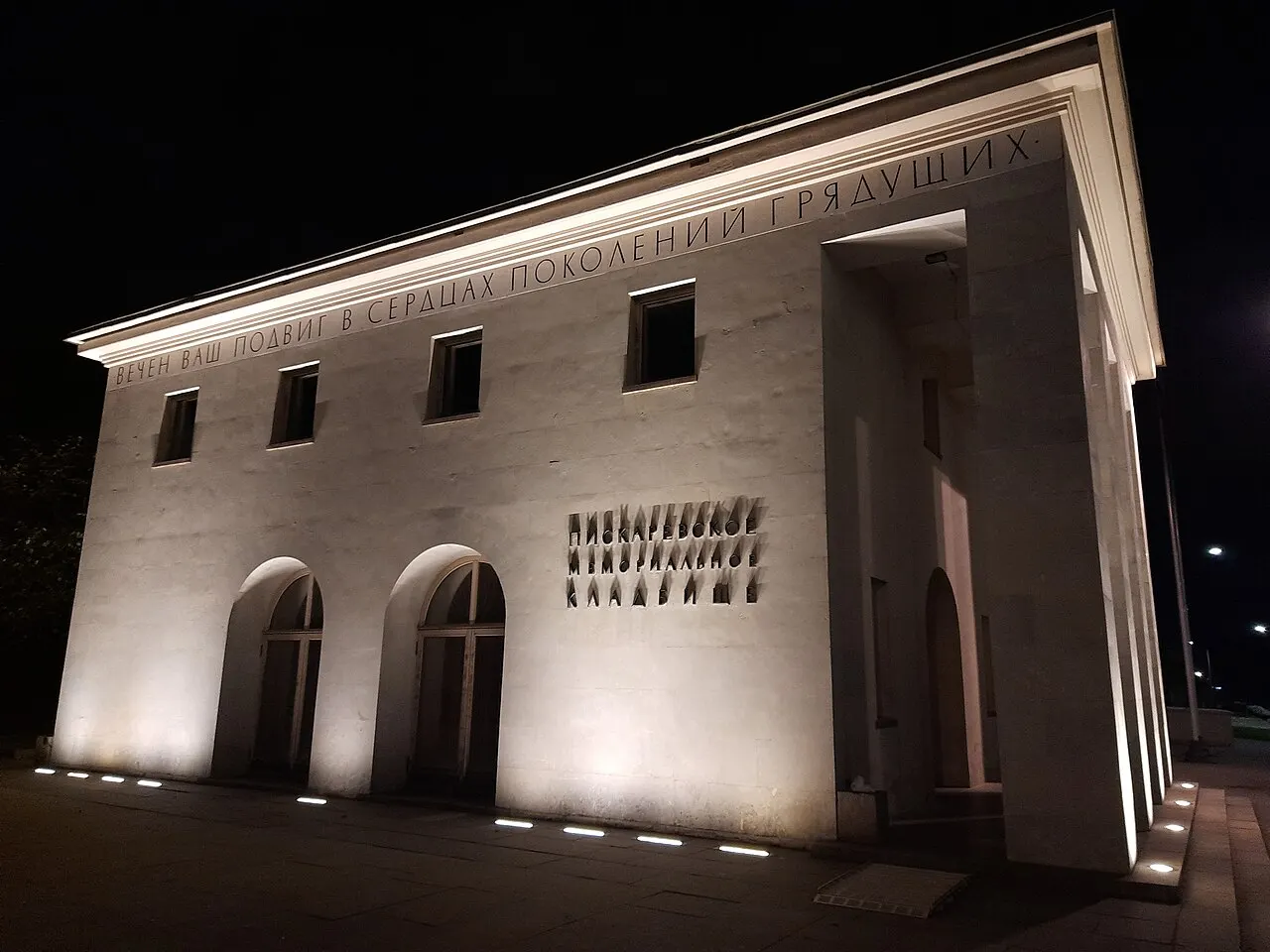 Pavilhão de pedra da entrada do Cemitério memorial de Piskariovskoie, em São Petersburgo, iluminado à noite.