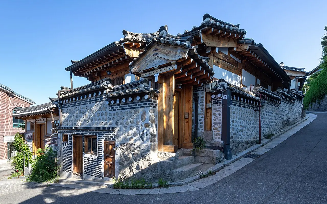 Casas tradicionais coreanas de telhado curvo e muros de pedra numa esquina em ladeira.