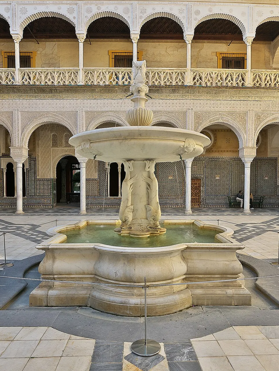 Fonte de mármore no centro do pátio principal da Casa de Pilatos, em Sevilha, com arcadas em volta.