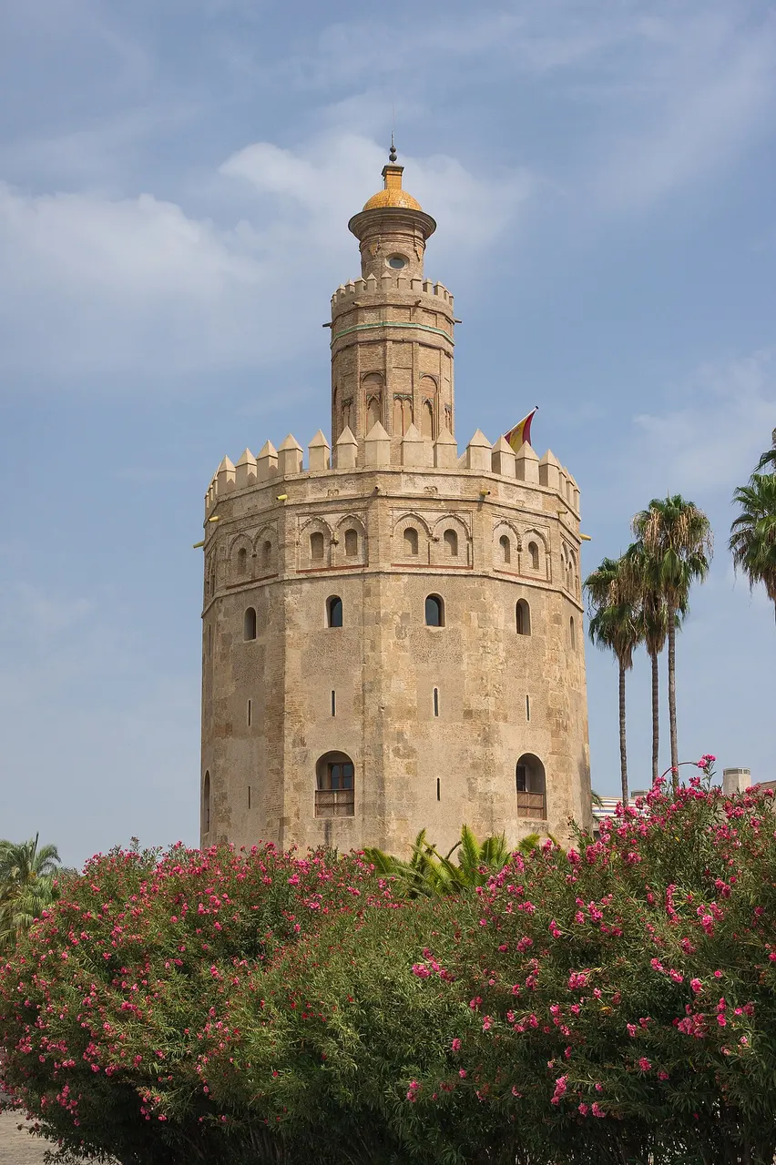 Torre del Oro, em Sevilha, torre de pedra de doze lados com a lanterna no alto, atrás de loureiros floridos.
