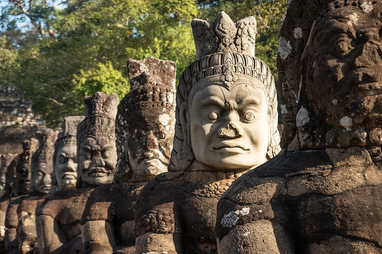 Estátua de pedra com um rosto sorridente esculpido no topo, numa fileira de estátuas iguais.