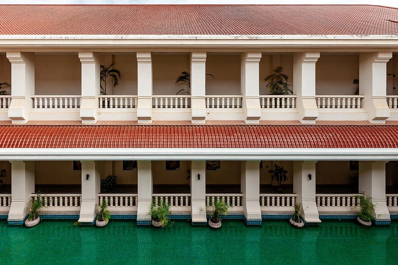 Galeria de dois andares do Museu Nacional de Angkor, com balaustrada branca, telhado vermelho e um espelho d’água.