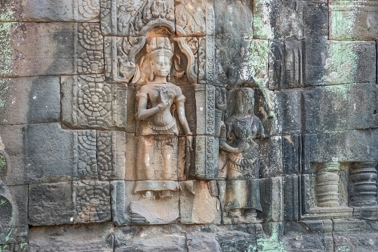 Figura feminina esculpida em relevo numa parede de pedra cinza, com coroa e colar.
