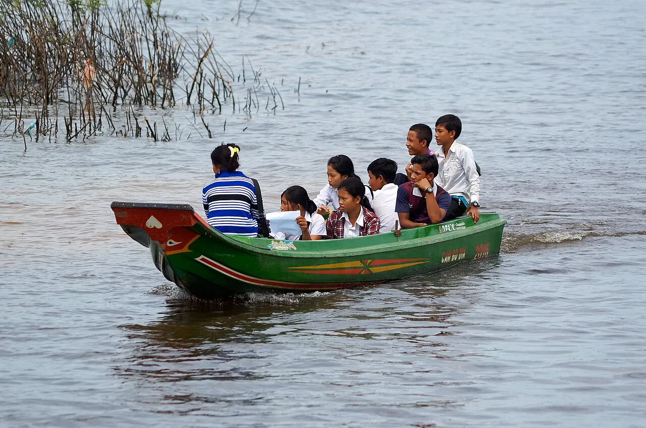 Barco comprido e estreito com várias crianças de uniforme branco sentadas em fila.