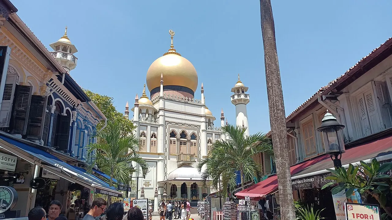 Mesquita branca com grande cúpula dourada e minarete, ao fim de uma rua de sobrados coloridos.