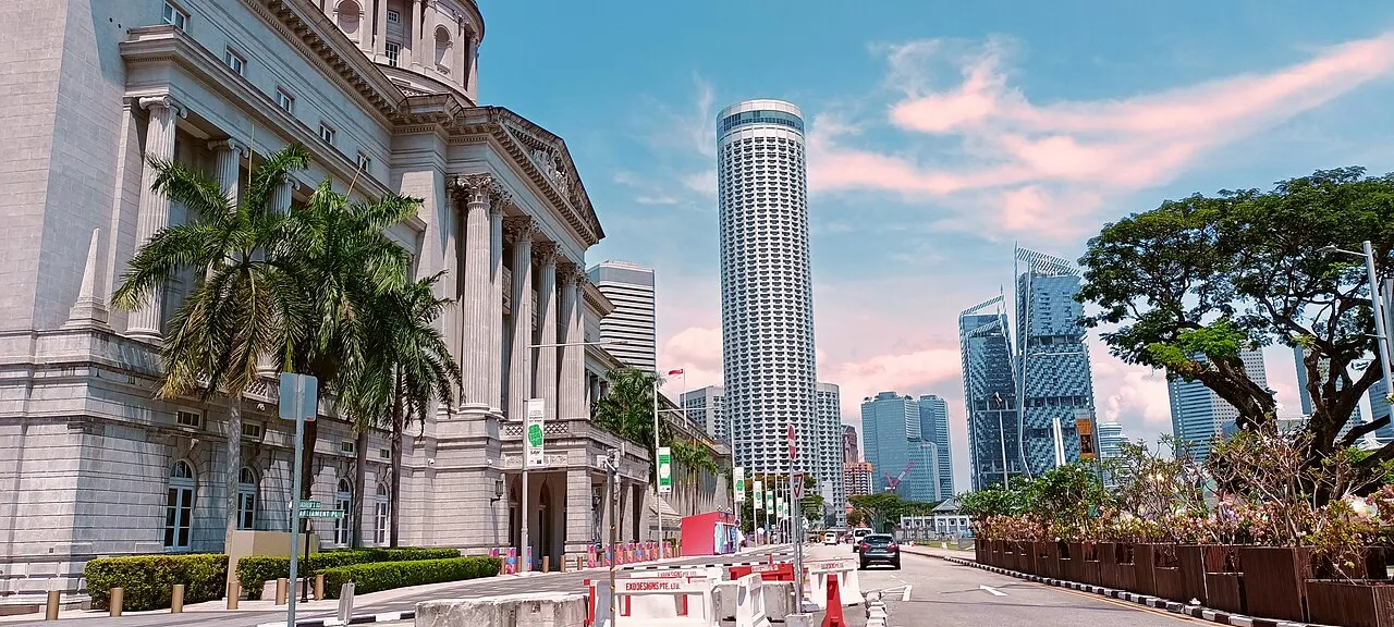Fachada neoclássica do edifício da National Gallery Singapore, com palmeiras na rua e arranha-céus ao fundo.