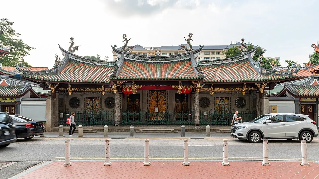 Fachada de templo chinês com telhado de beirais curvos e ornamentos em relevo, com carros estacionados à frente.