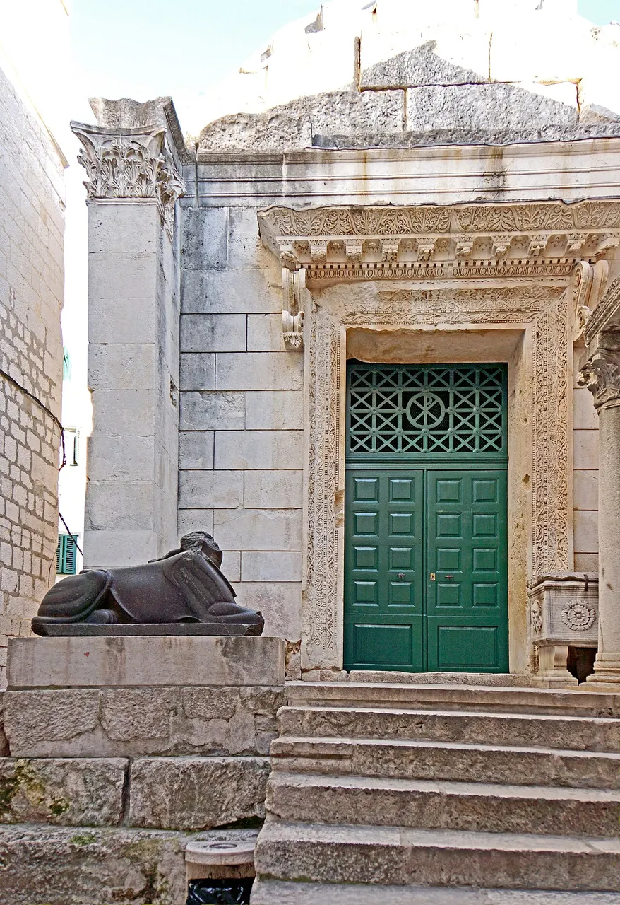A porta verde do Templo de Júpiter, com moldura de pedra esculpida, e uma esfinge de granito escuro ao lado da escada.