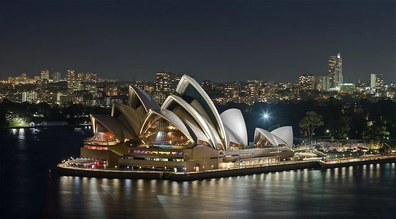 As conchas iluminadas da Sydney Opera House vistas da baía, à noite.