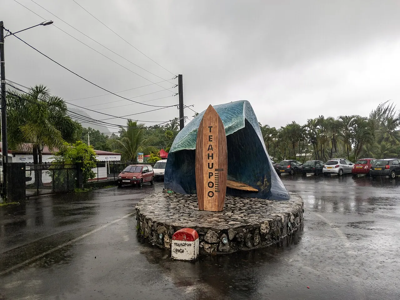 Monumento em forma de onda com uma prancha com o nome Teahupoo, sobre base de pedra, num dia de chuva.