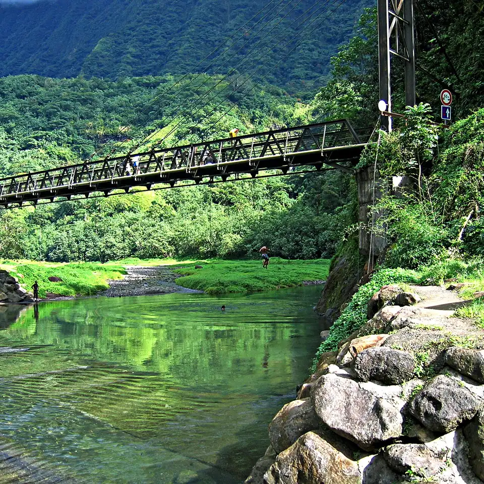 Rio verde entre paredões de floresta, com uma ponte de metal ao fundo.