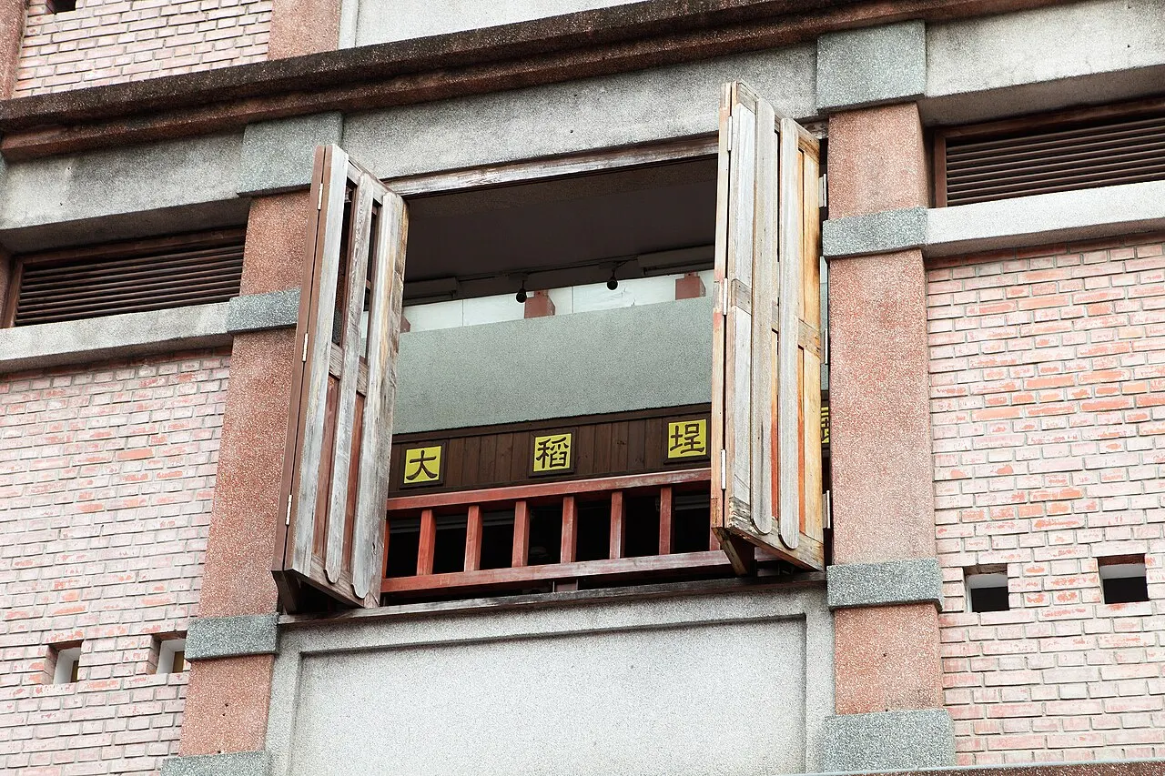 Veneziana de madeira dobrável, aberta sobre uma fachada de tijolos, revelando um letreiro dourado.