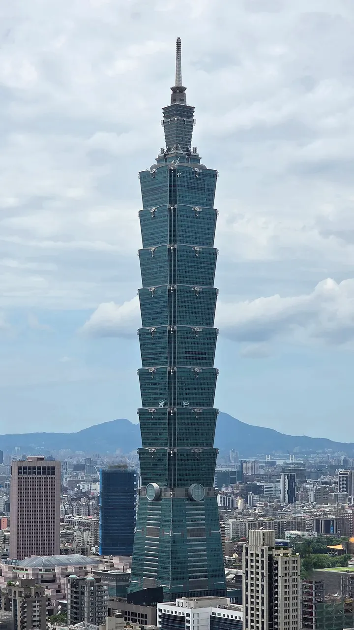 Arranha-céu esguio e verde-azulado, em segmentos empilhados como bambu, entre outros prédios da cidade.