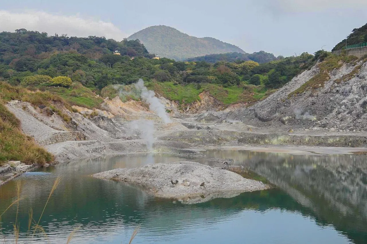 Fumarolas e um lago em um vale vulcânico de Yangmingshan, com encostas de rocha clara e morros verdes ao fundo.