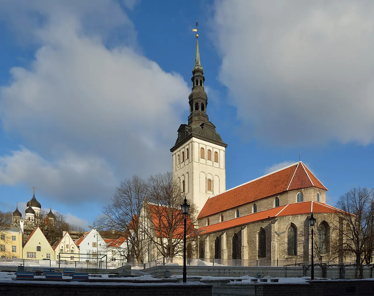 Igreja de São Nicolau, em Tallinn, de paredes claras, telhado vermelho e torre com agulha escura.
