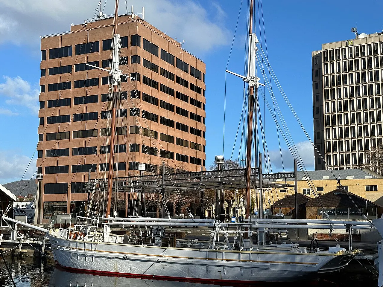 An old white-hulled two-masted sailing ship moored in Constitution Dock, with office buildings of central Hobart behind.