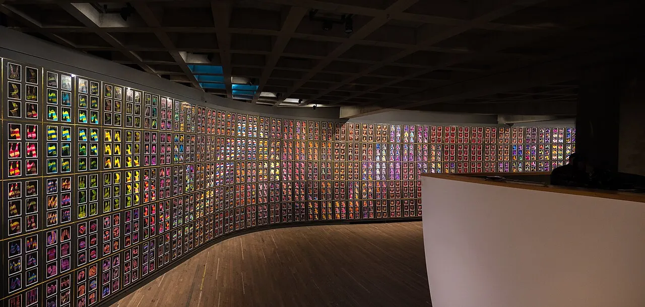 A dark gallery at MONA, with a curved wall covered in hundreds of small colourful panels and a wooden floor.