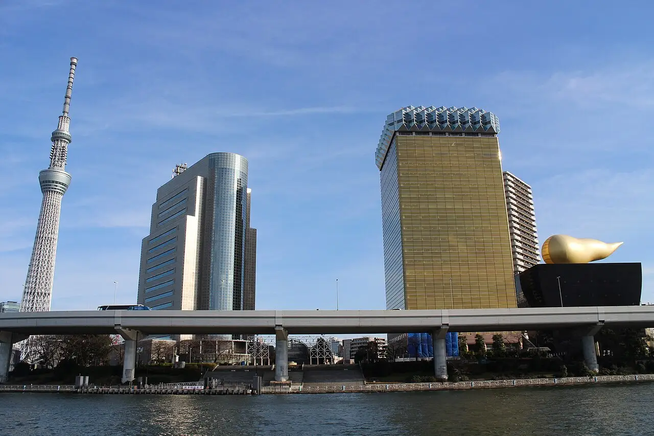 Torre branca alta ao lado do rio, com a chama dourada do prédio Asahi à direita.