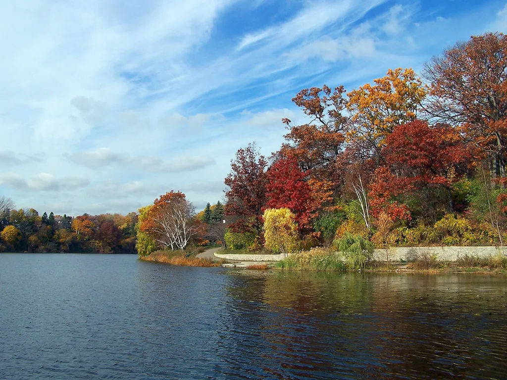 El Grenadier Pond, en High Park, con árboles rojos y amarillos de otoño en la orilla y cielo azul.