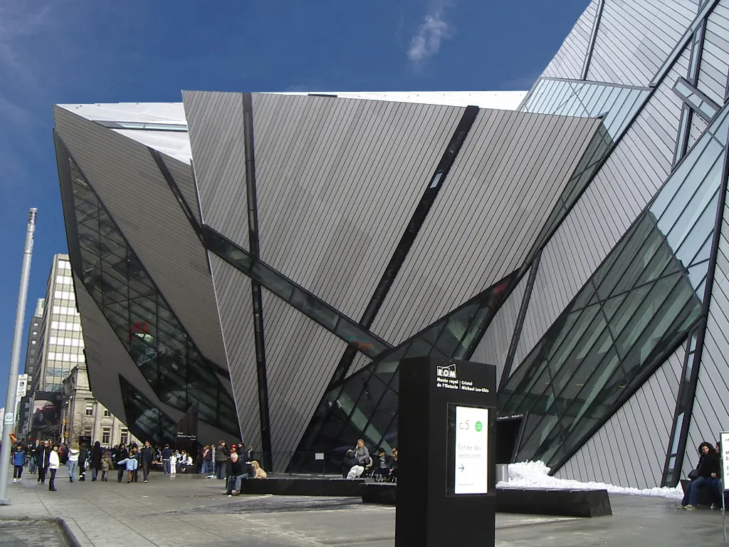 Los prismas inclinados de aluminio y vidrio del Michael Lee-Chin Crystal, anexo del Royal Ontario Museum, sobresaliendo sobre la acera en un día de cielo azul, con nieve y peatones abajo.