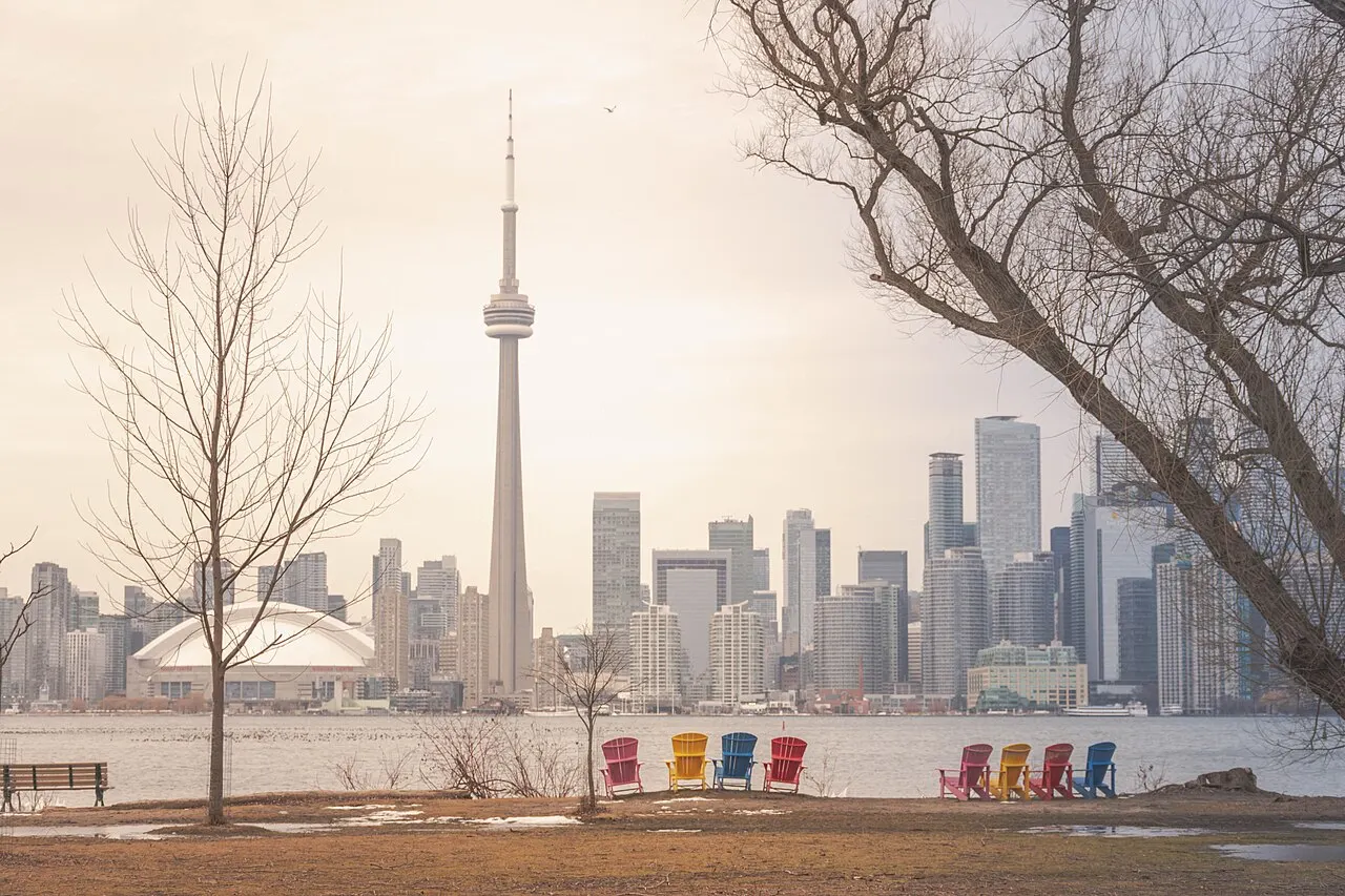 Sillas de colores en la orilla de las Toronto Islands, frente al horizonte de Toronto con la CN Tower al centro, bajo un cielo despejado de invierno.