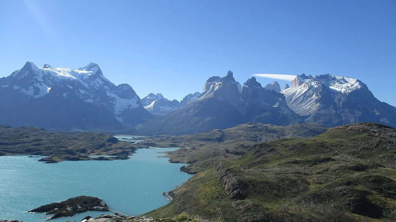 A vista do Mirador Cóndor: o Lago Pehoé turquesa embaixo, ilhotas e o maciço do Paine nevado em toda a largura, sob céu azul.