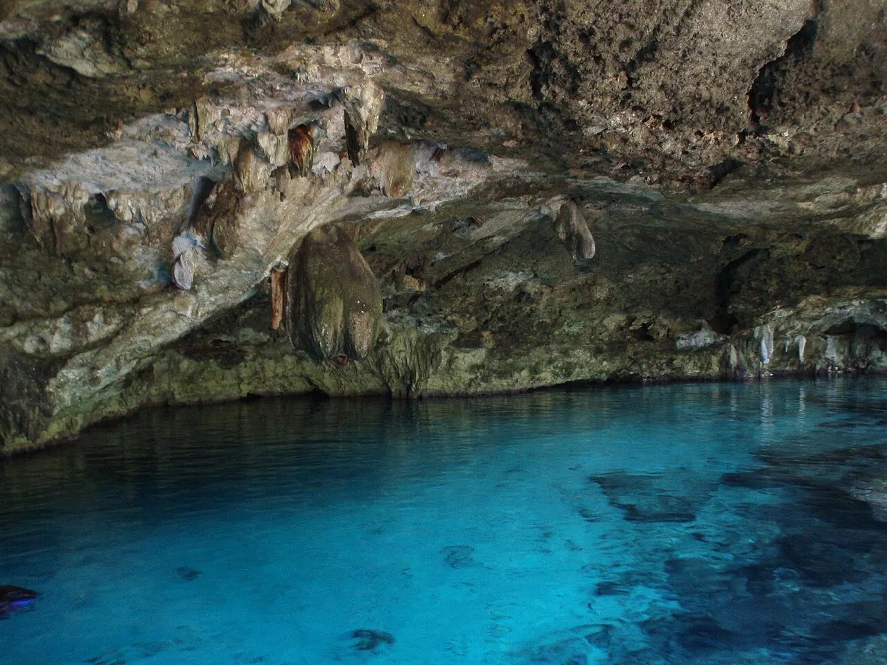 Entrada da caverna do cenote Dos Ojos, com água azul e estalactites no teto de rocha.