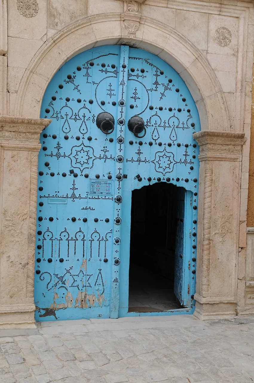 Porta de entrada azul, com cravos pretos e arco de pedra, do palácio Dar Ben Abdallah na medina de Túnis.