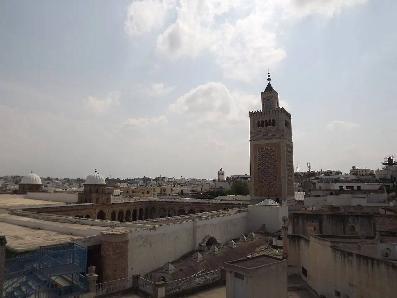 Minarete quadrado da Mesquita Zitouna acima dos telhados da medina de Túnis, sob céu com nuvens.
