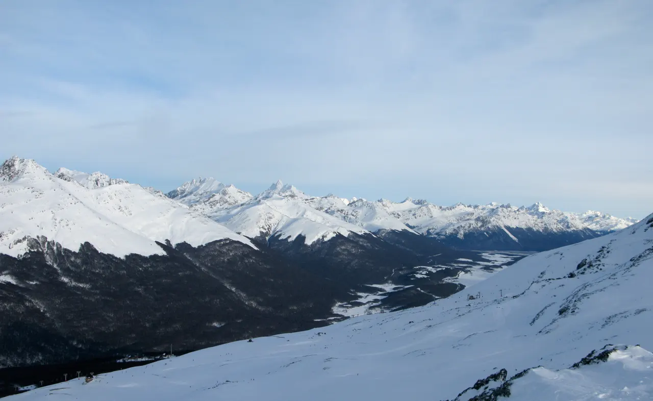 Vista do Cerro Castor, com encosta coberta de neve e cadeia de montanhas de cumes brancos ao fundo.