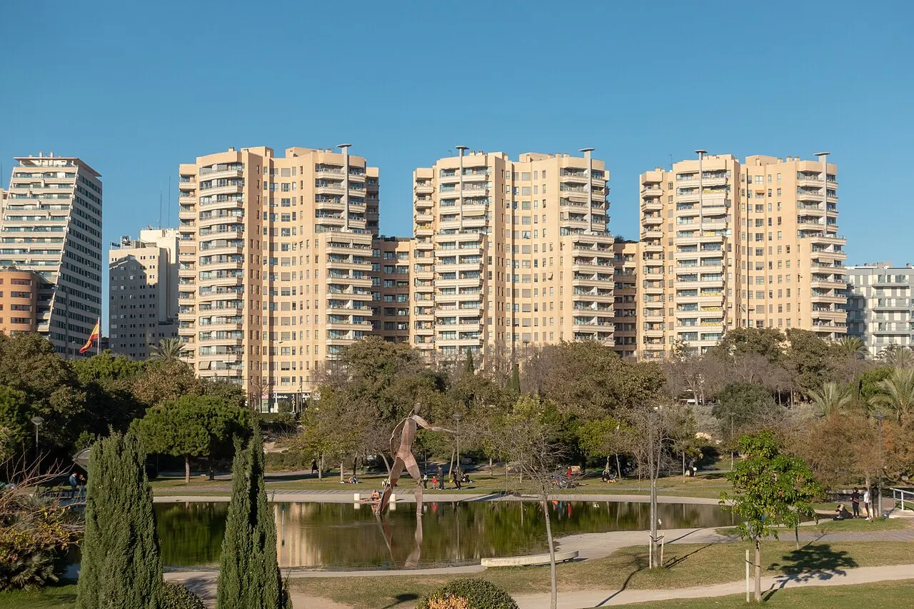 Um trecho do Jardín del Turia, no antigo leito do rio, com árvores, um lago e prédios residenciais altos na margem.