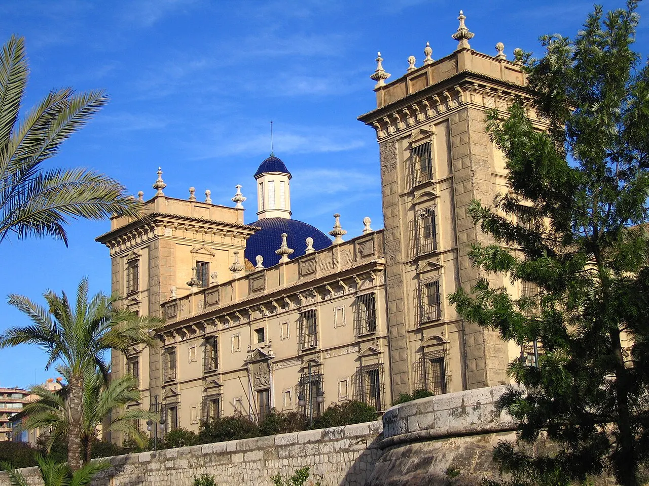 O prédio do Museo de Bellas Artes de Valência, antigo seminário de pedra clara com torres e cúpula azul, entre palmeiras.