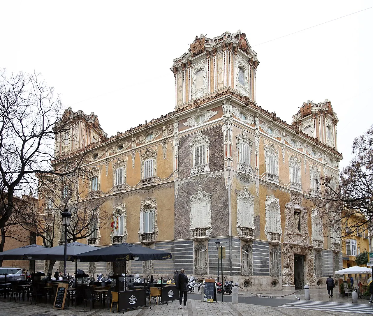 O Palácio do Marquês de Dos Aguas, sede do Museo Nacional de Cerámica, com fachada pintada e torres de canto, numa esquina com mesas na calçada.