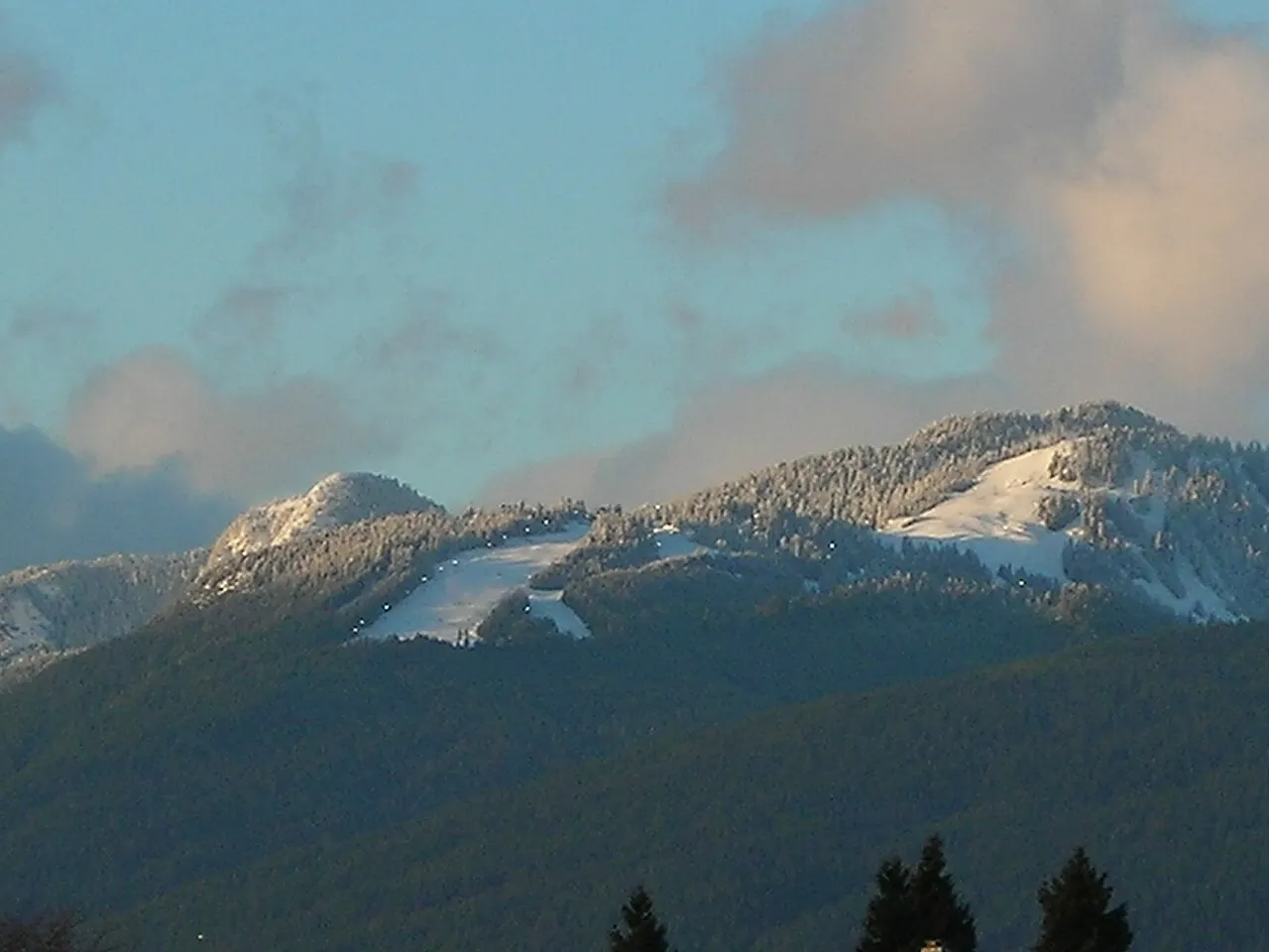 A Grouse Mountain, com pistas de esqui abertas na encosta coberta de mata, sob céu de fim de tarde.