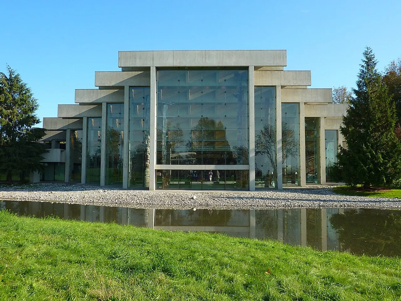 Museu de Antropologia da UBC, em Vancouver, com a fachada de vidro e vigas de concreto, diante do espelho d'água.